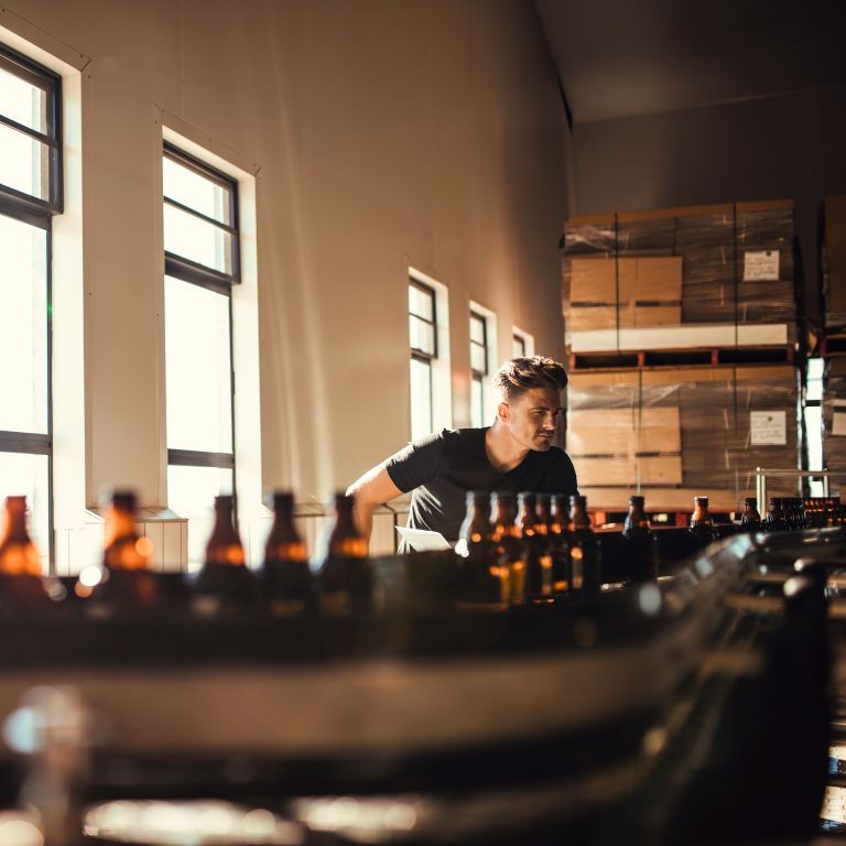 Worker monitoring glass bottles on a production line in a food and beverage facility during a product recall process