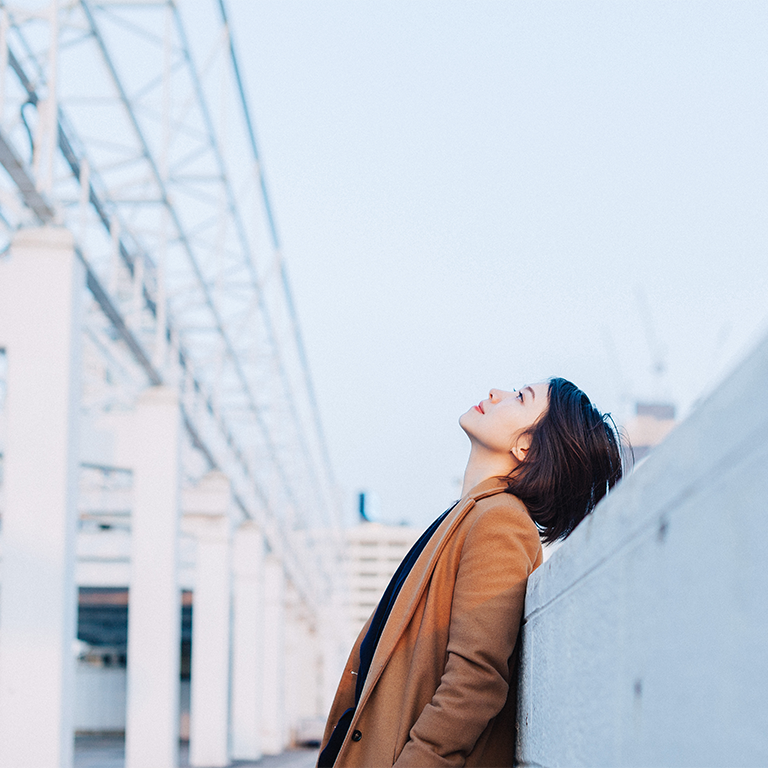Person leaning against a concrete wall on an urban rooftop with structural columns and pale sky, image for burnout at work.