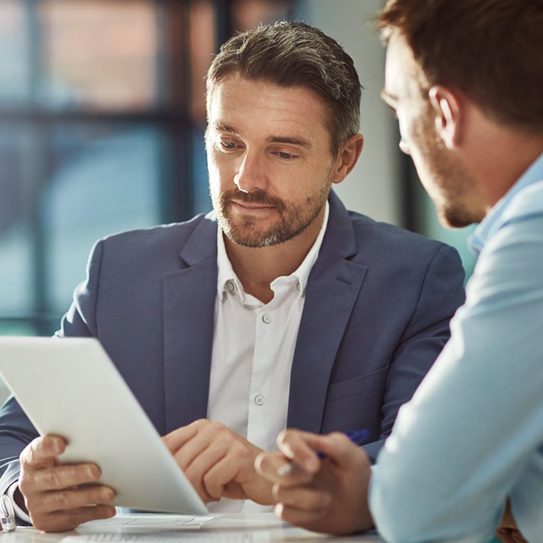 Two professionals discussing a tablet in a modern office setting, highlighting the impact of national insurance increases on business operations.