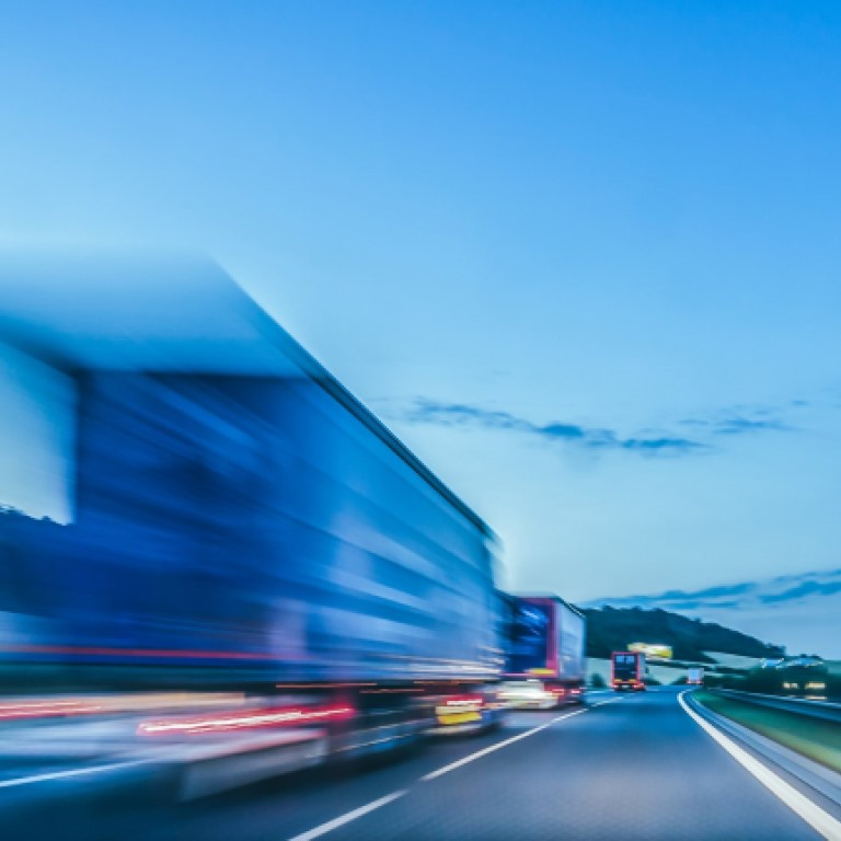A blurred image of trucks driving on a highway during twilight, illustrating the importance of motor fleet insurance for commercial vehicles.