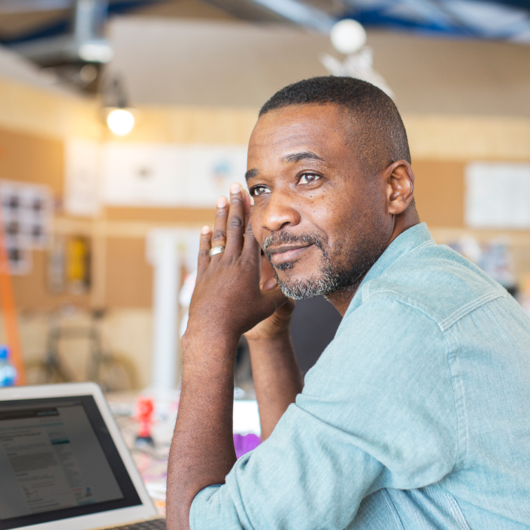 A man in a light blue shirt working on a laptop in a modern office environment, representing small business engagement with cybersecurity measures under the Cyber Bill for SMEs