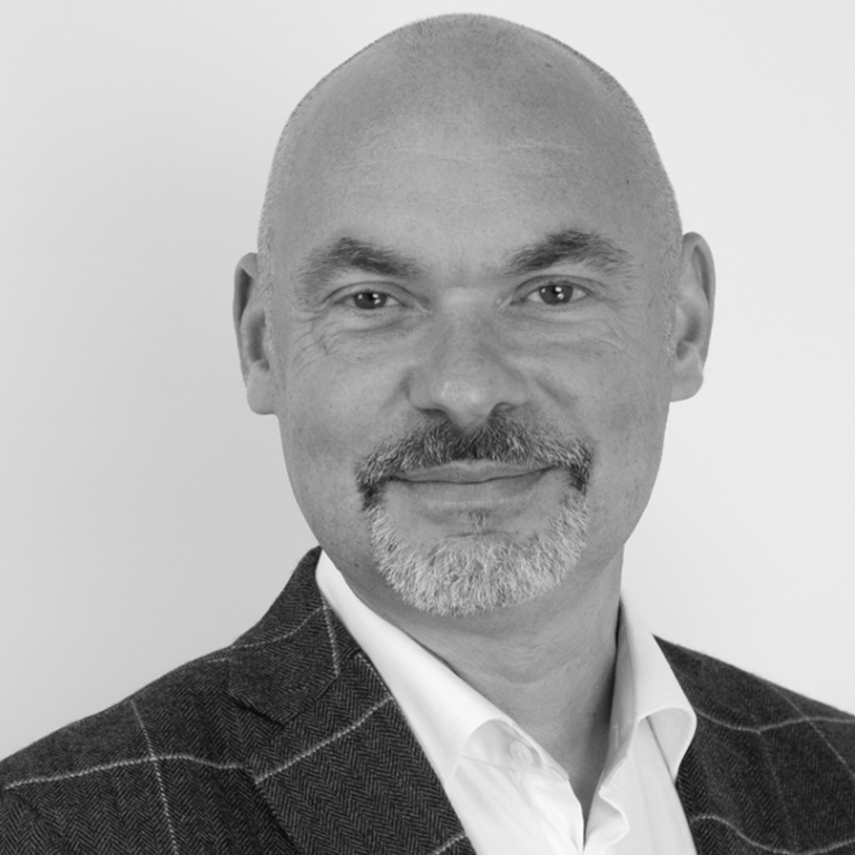 Black and white professional headshot of Paul Martin wearing a checkered blazer and white shirt, facing forward against a plain background.