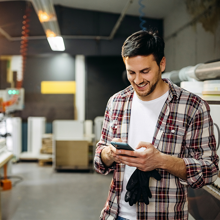 A business owner in a workshop environment checks his smartphone, illustrating the use of trade credit in managing operations within a BANI economy.
