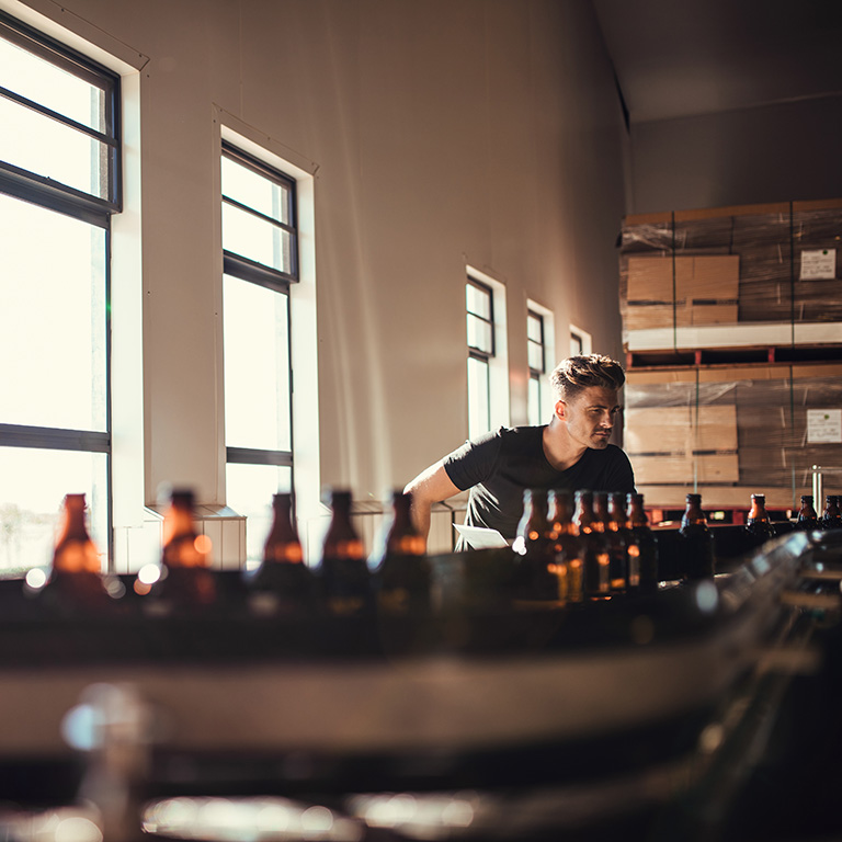 A worker inspecting bottles on a production line in a food and beverage manufacturing facility, illustrating the importance of trade credit insurance for the food and beverage industry